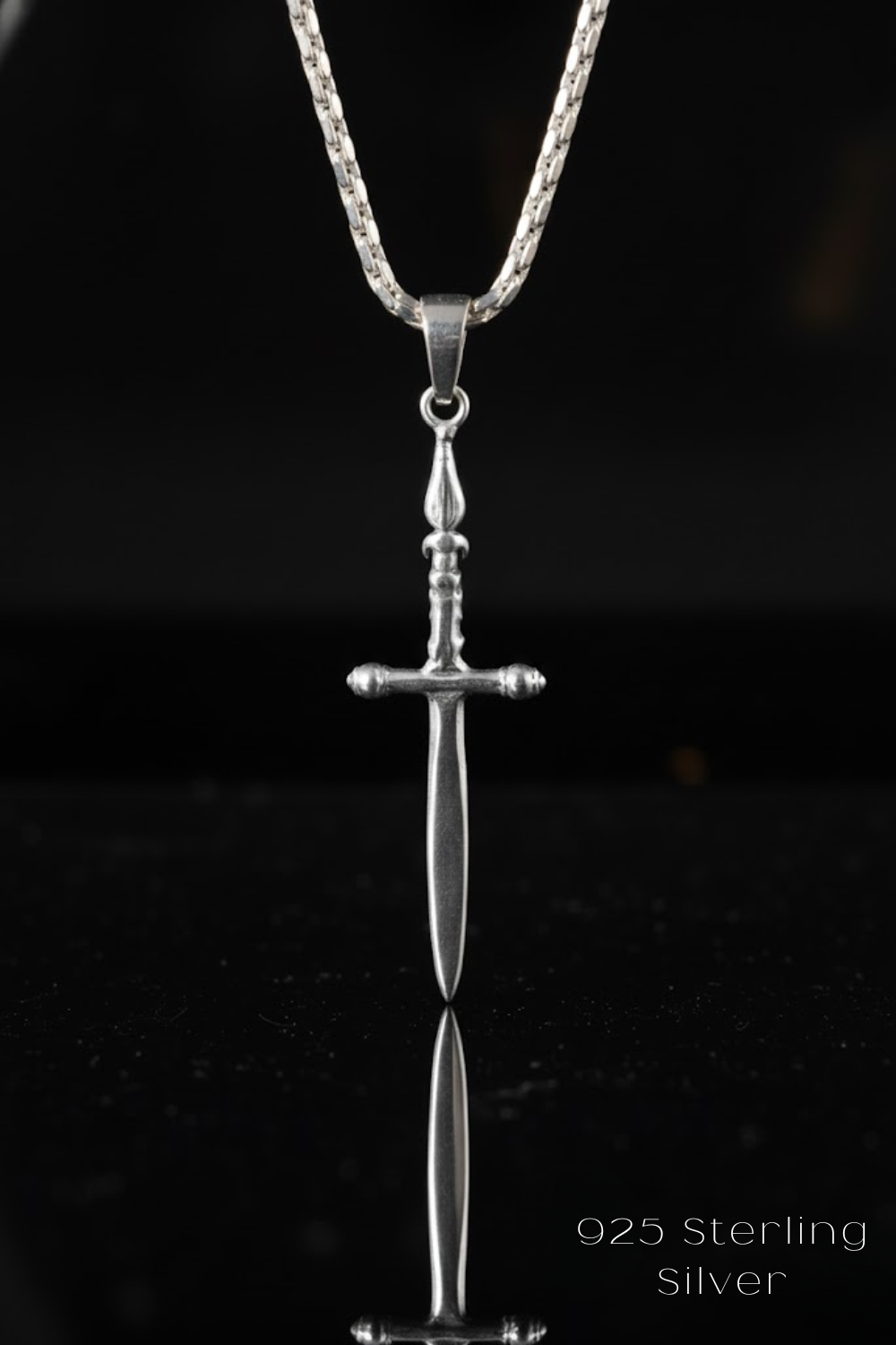 A silver-colored pendant with a cross-shaped design, suspended from a chain against a black background.
