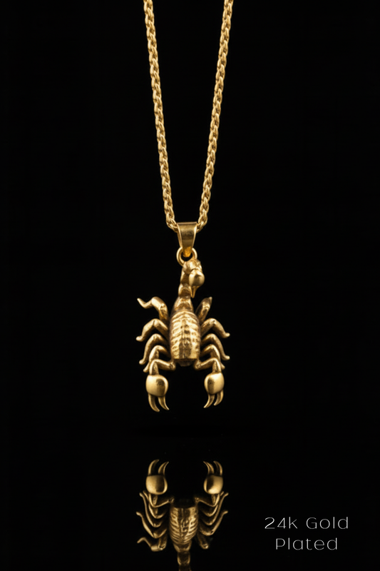 A 24k gold plated pendant in the shape of a scorpion is displayed against a black background, with its reflection visible below it.