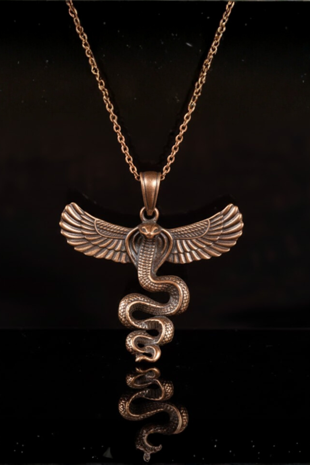 A gold-colored pendant necklace with a snake design, featuring a snake's head and a snake's body with wings.