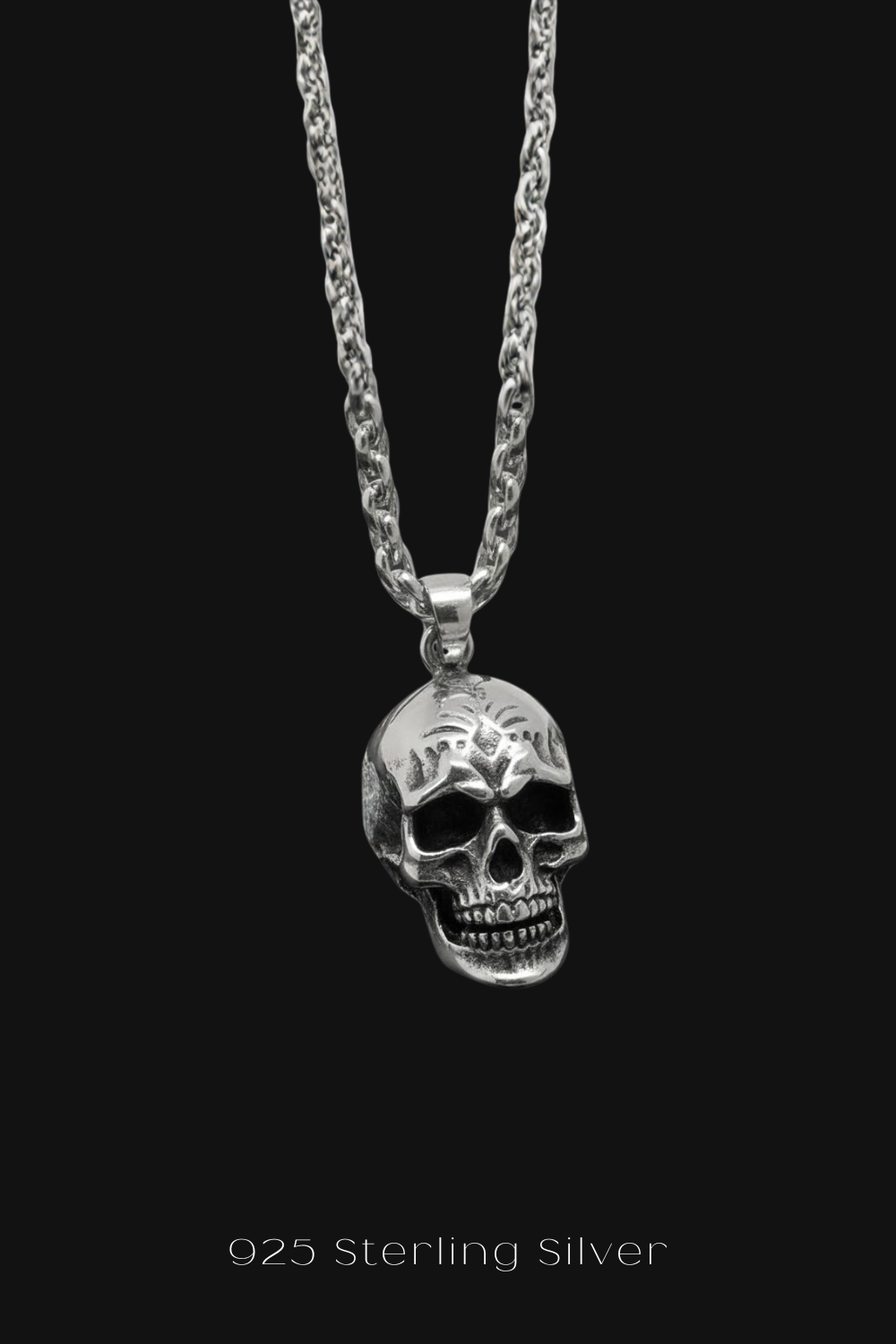 A silver-toned pendant necklace with a skull pendant is displayed against a black background.
