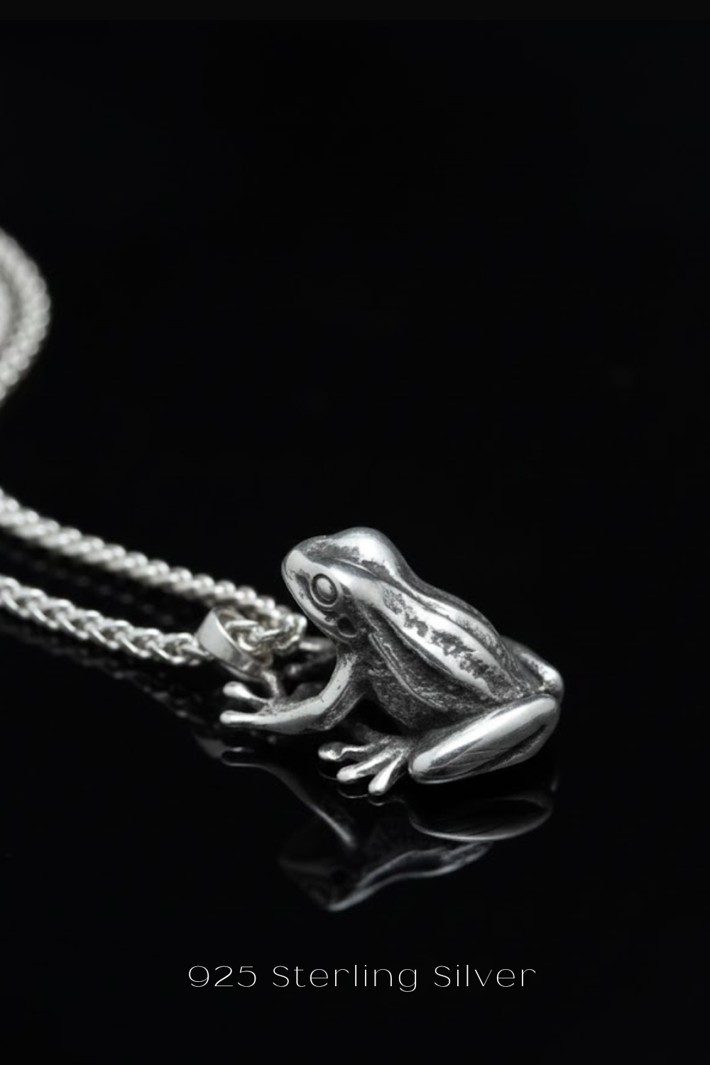 A silver frog pendant necklace against a black background.