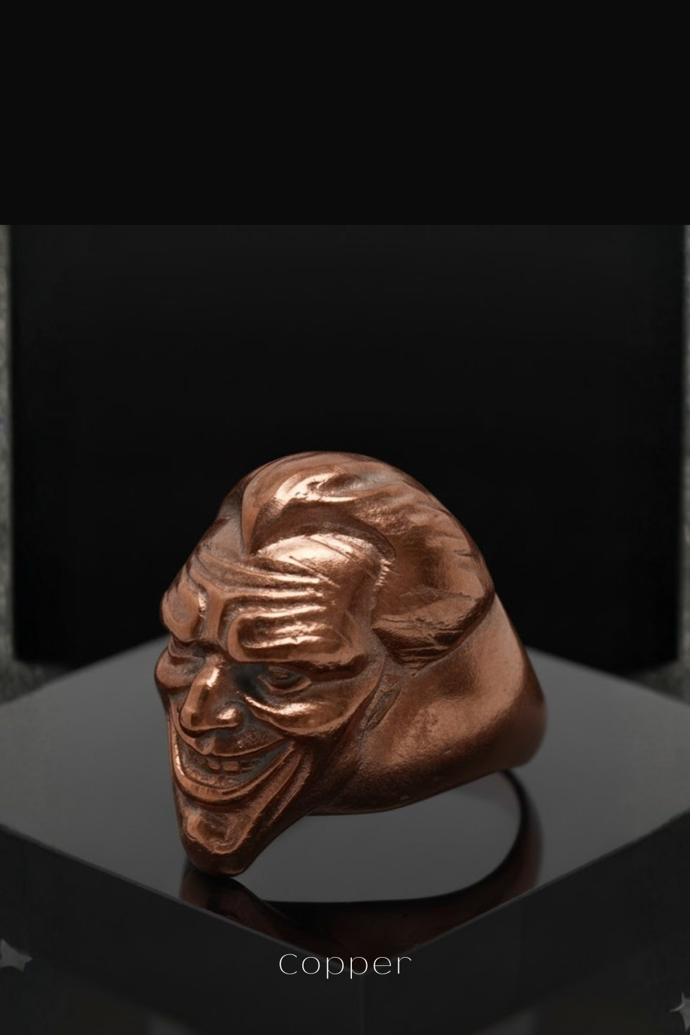 A copper-colored metal sculpture of a smiling, twisted face is displayed on a black surface.