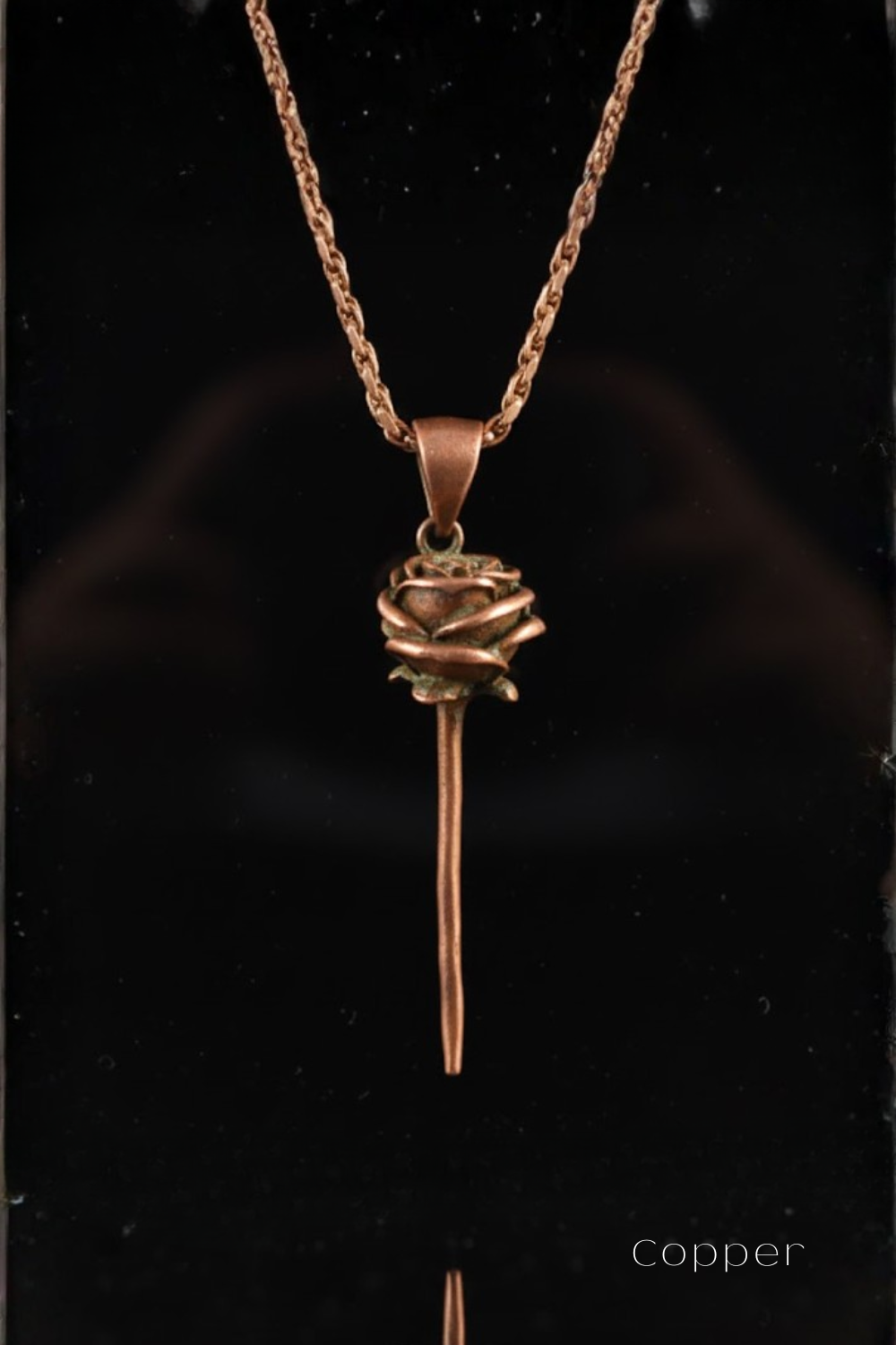 A copper-colored pendant necklace with a rose-shaped charm hanging from it.