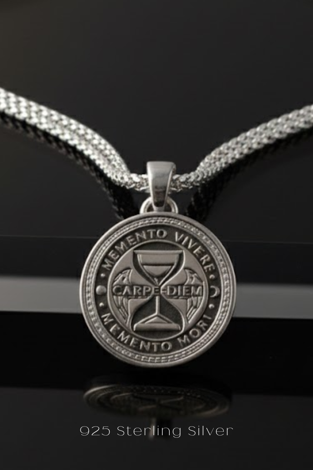 A silver pendant necklace with a circular medallion featuring the Latin motto "Memento Víverre" and the words "CARPEDIEM" and "MEMENTO MORI".