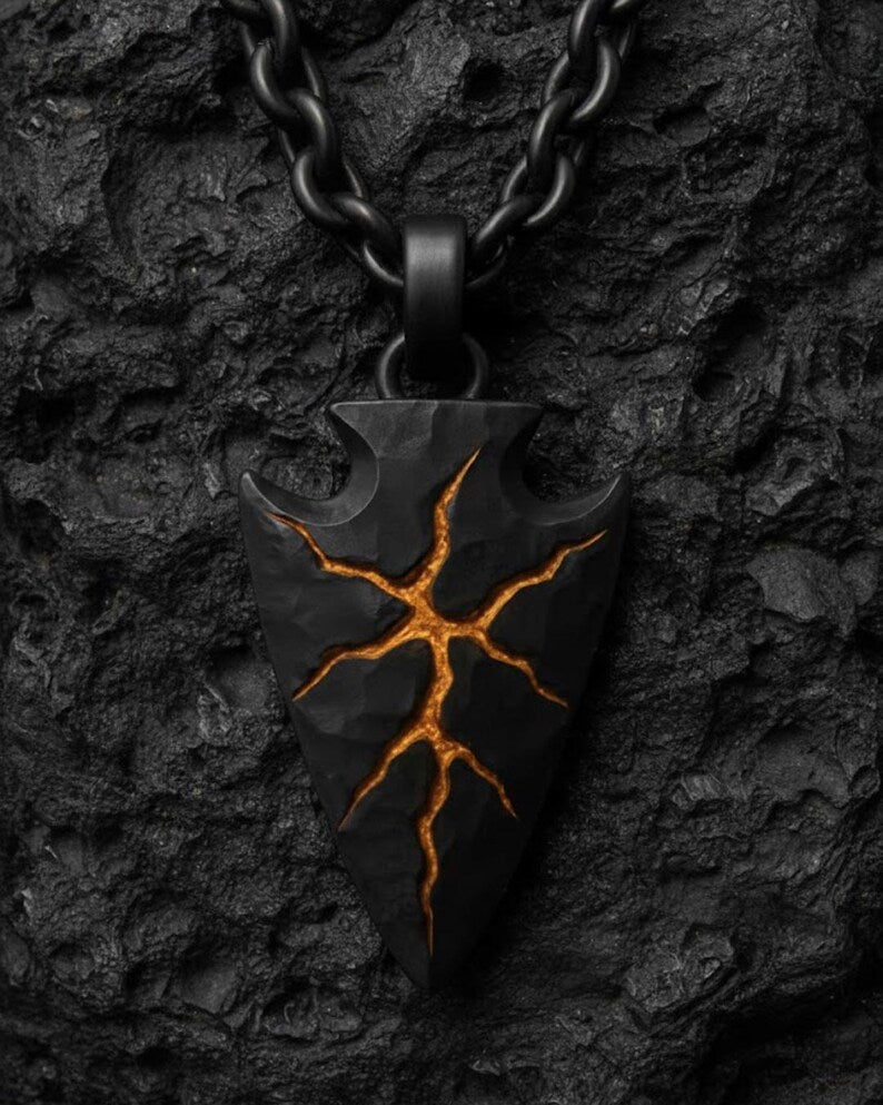 A black pendant with a striking design, featuring a cracked arrowhead shape with a fiery orange glow at the center.