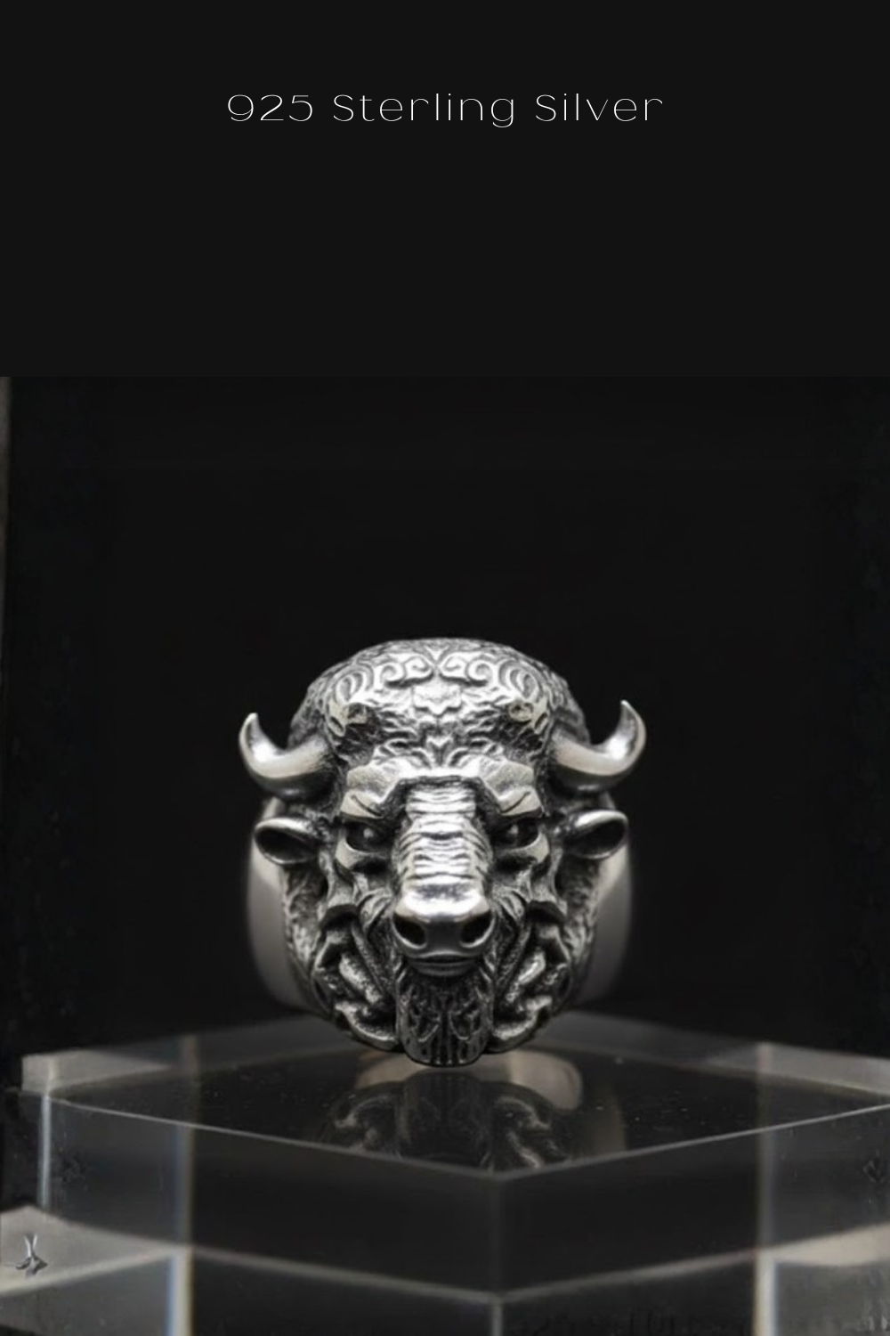 A silver ring featuring a detailed buffalo head design, with horns and a snout, is displayed on a clear glass stand against a black background.