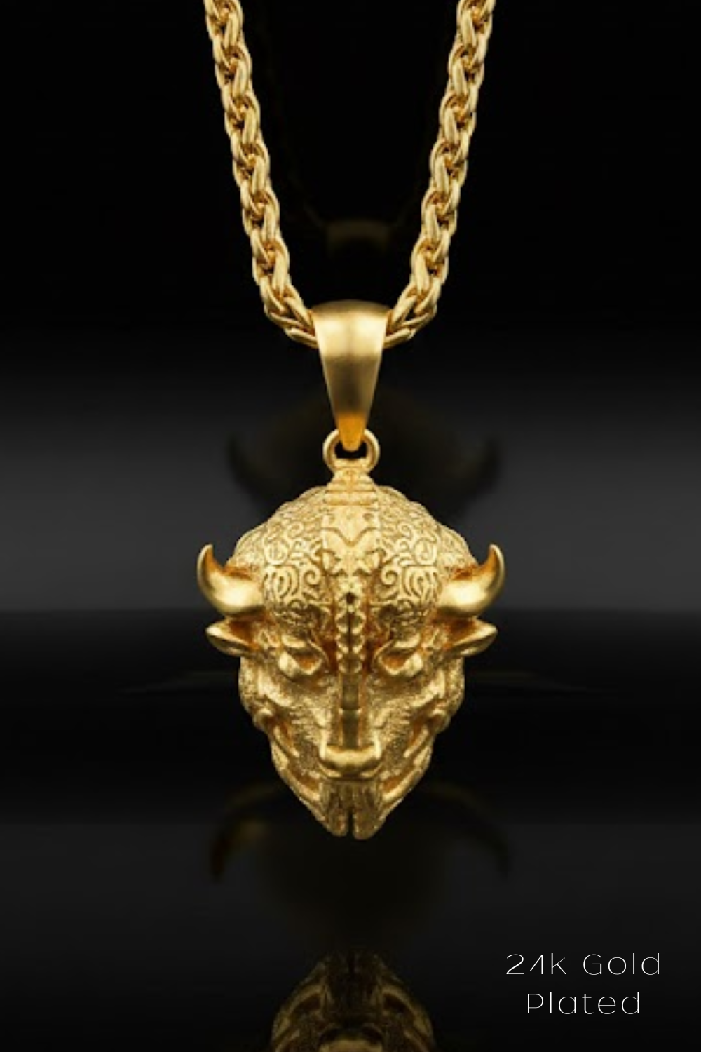 A 24k gold plated pendant in the shape of a bull's head is displayed against a black background.