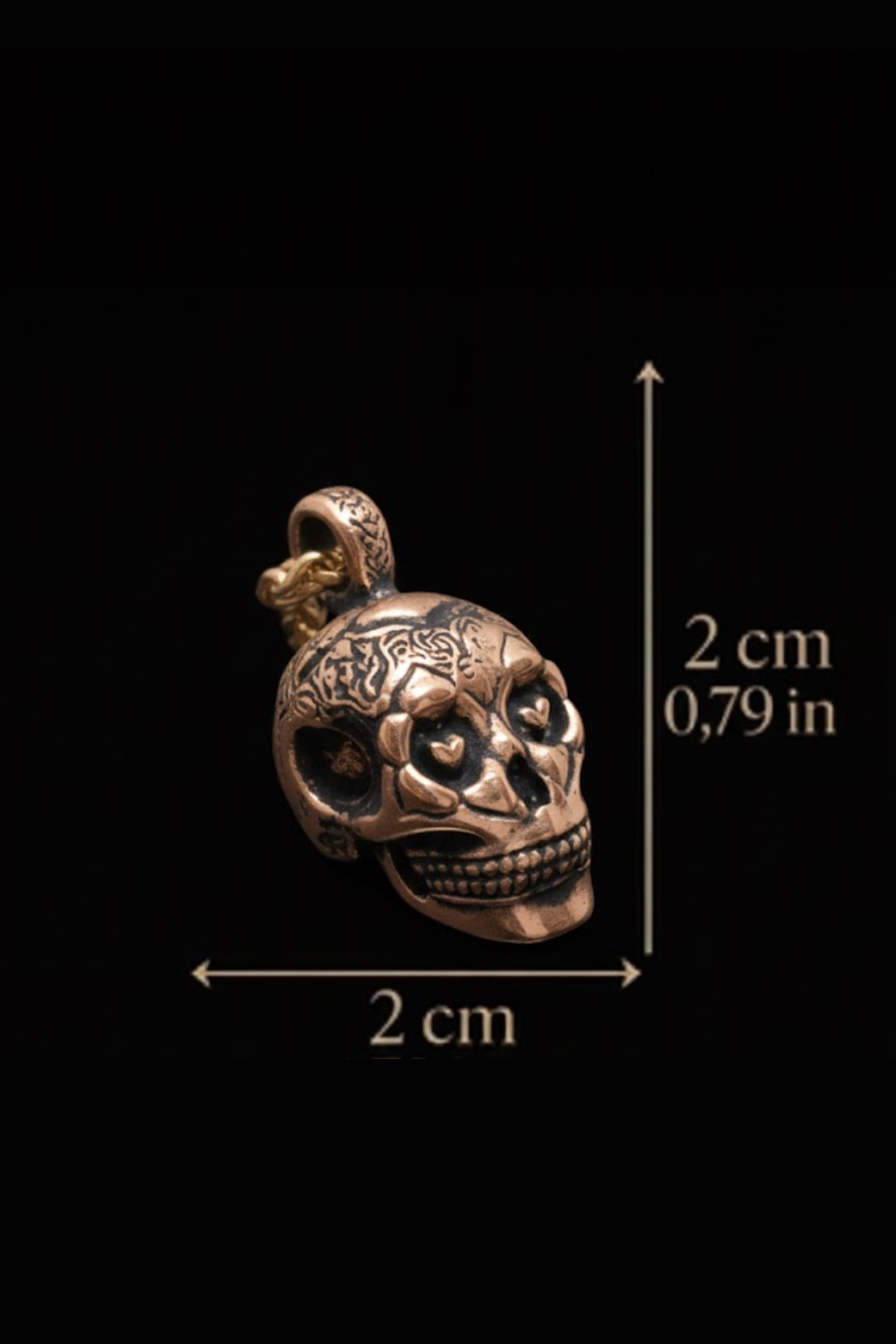 A close-up image of a metal skull pendant with intricate designs, accompanied by a scale indicating its size.