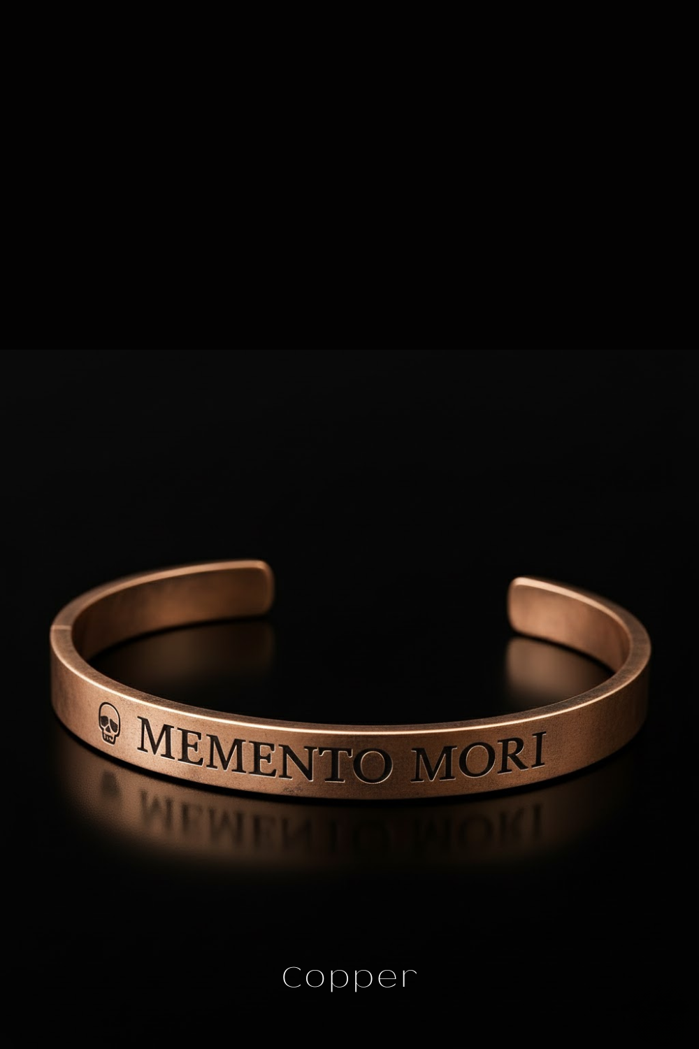 A copper-colored bracelet with the text "MEMENTO MORI" engraved on it, against a black background.