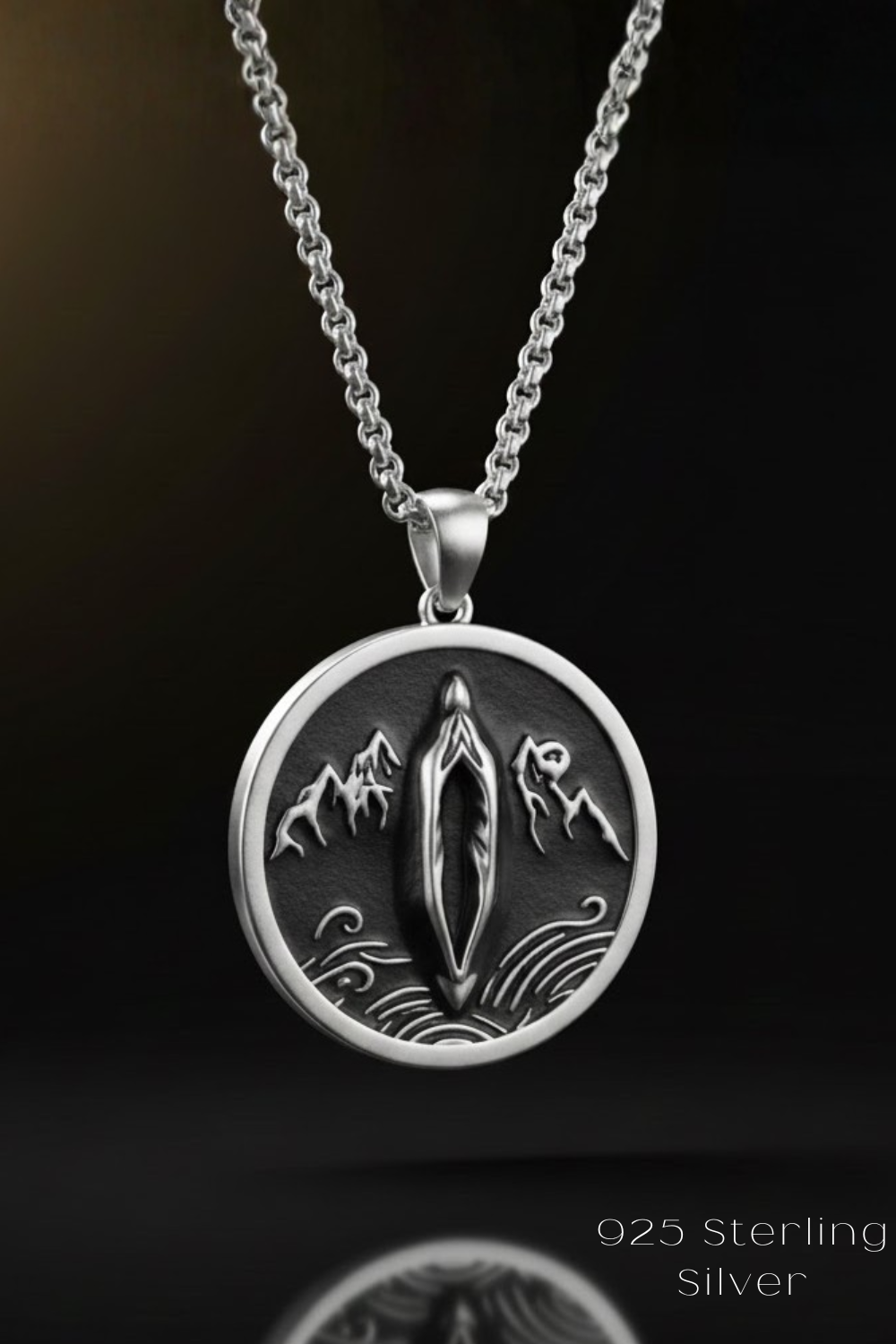 A silver necklace pendant with a circular design featuring a figure of a person and mountains.