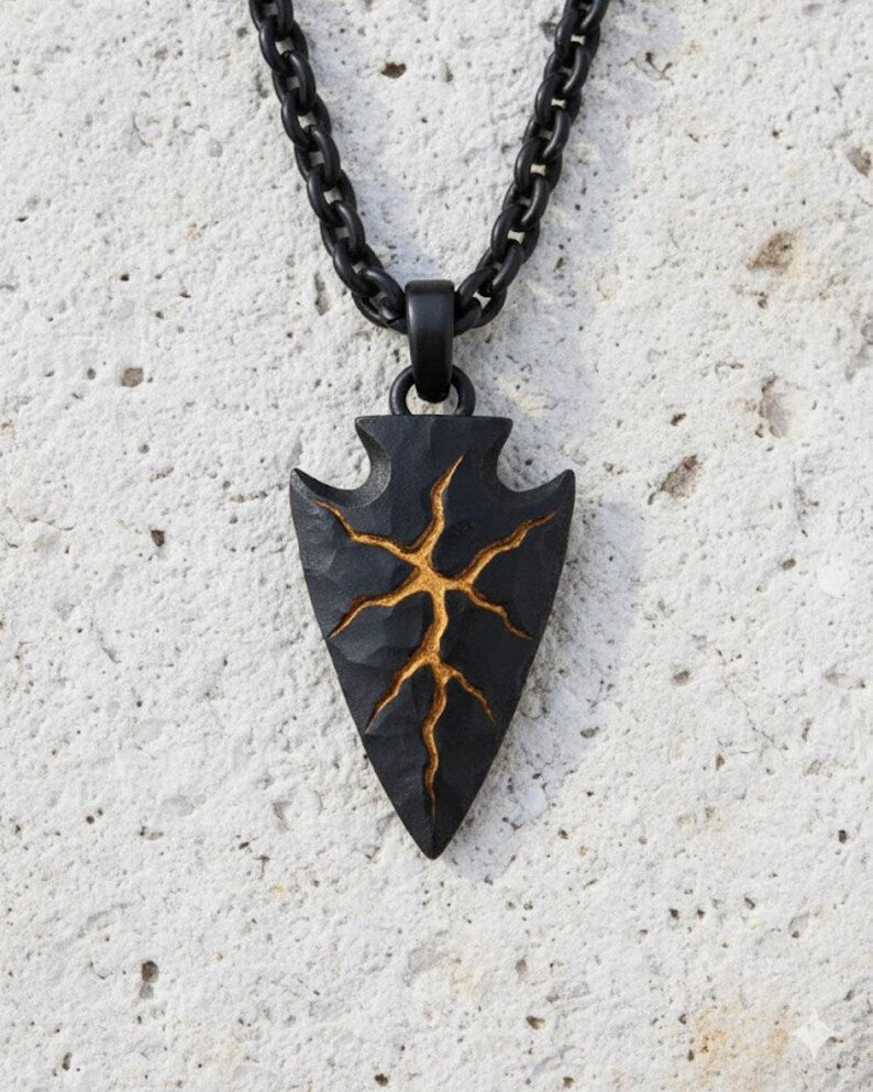 A black pendant with a gold design on it, hanging from a chain against a white background.