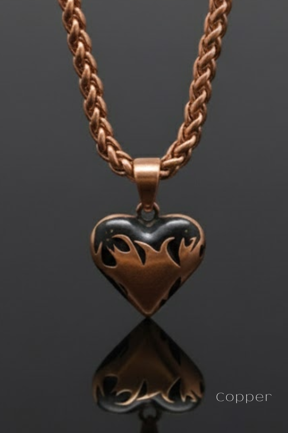 A copper-colored heart-shaped pendant with a flame design, suspended from a chain against a dark background.