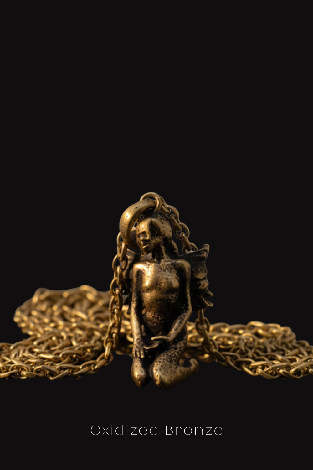 a close-up view of a small, bronze-colored pendant or sculpture with a chain or necklace attached to it, set against a black background.