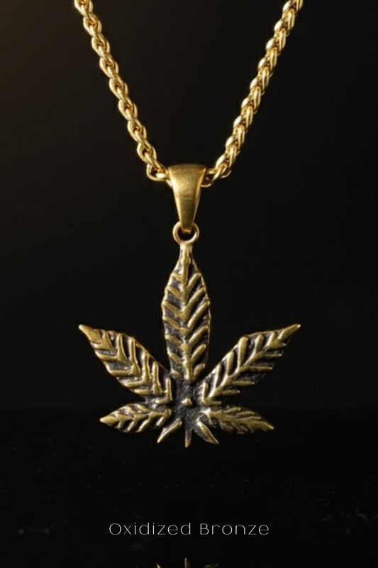A gold-colored pendant necklace with a detailed leaf-shaped pendant in the center, set against a black background.