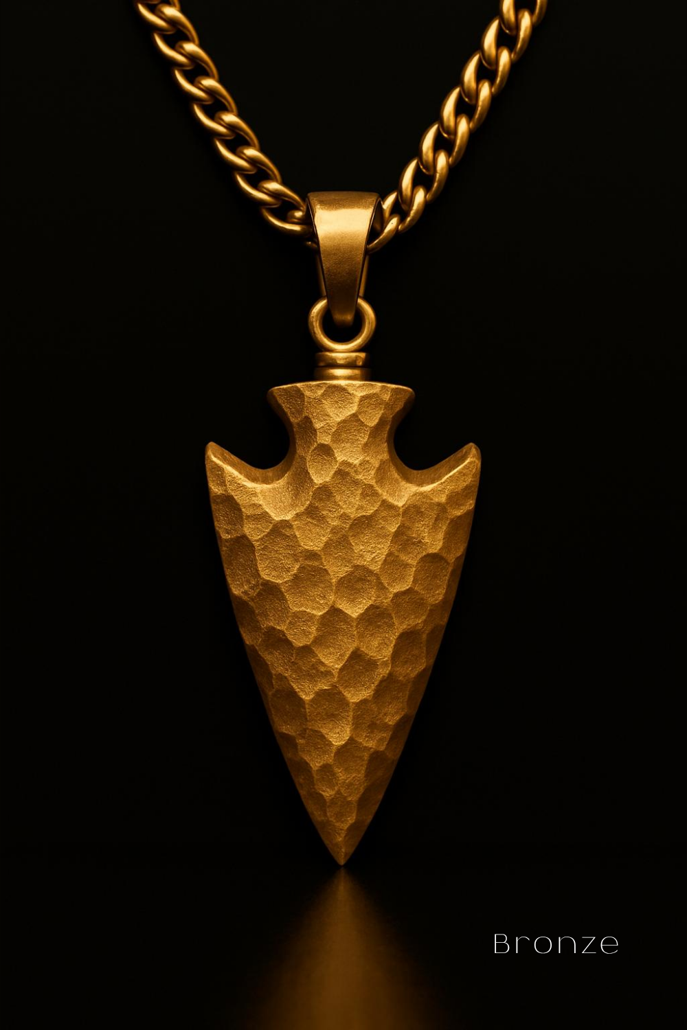 A close-up view of a gold-colored pendant in the shape of an arrow, with a chain around it, against a black background.