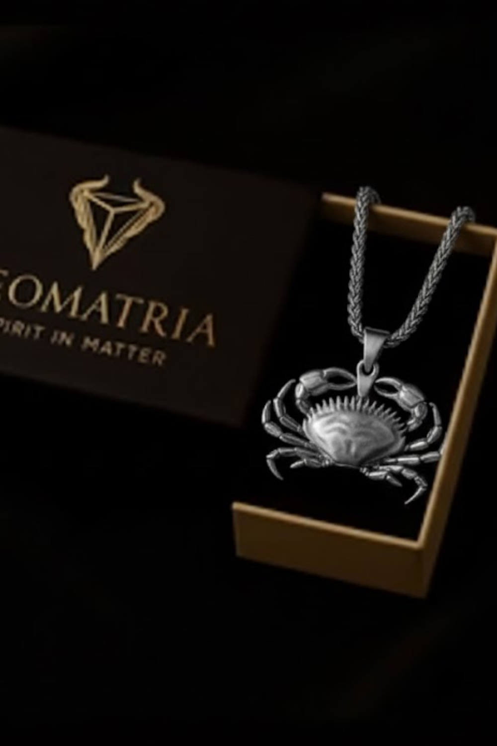 a silver crab pendant necklace displayed in a wooden box with the brand name "SOMATRIA" printed on it.