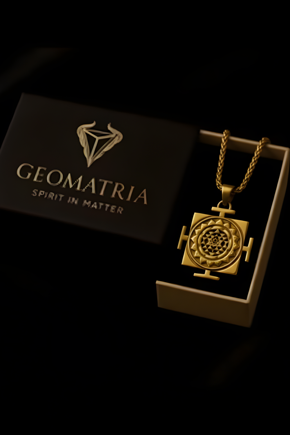 A gold necklace with a pendant is displayed in a black box with the Geomatria logo, accompanied by a gold chain.