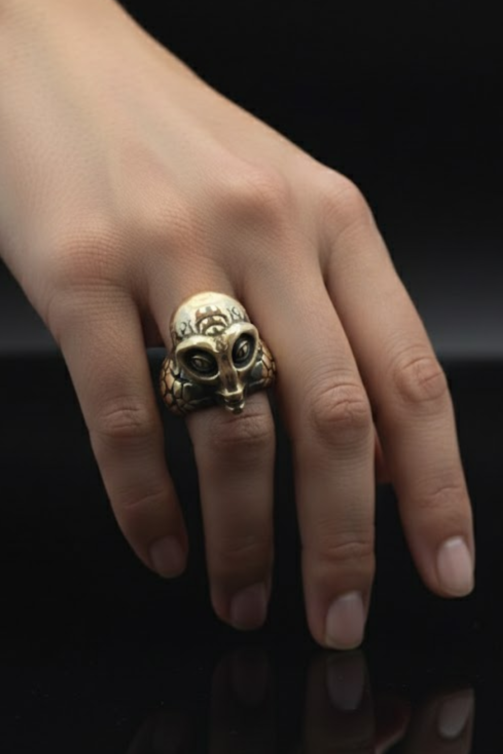 A close-up of a person's hand wearing a gold ring with an alien or alien-like face design.