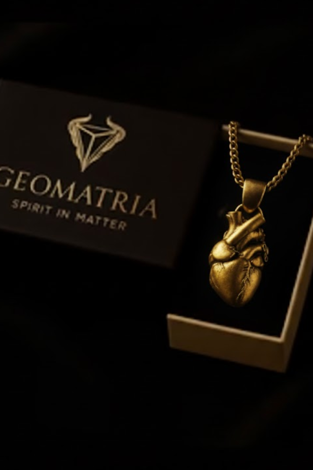 a gold heart-shaped pendant hanging from a chain, displayed in a box with the Geomatria brand name.