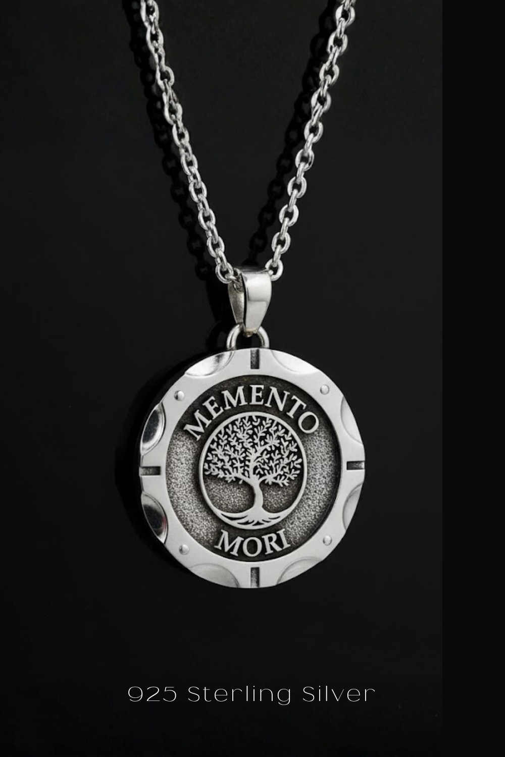 A silver necklace pendant with the Latin phrase "MEMENTO MORI" engraved on it, which means "Life begins" in English.