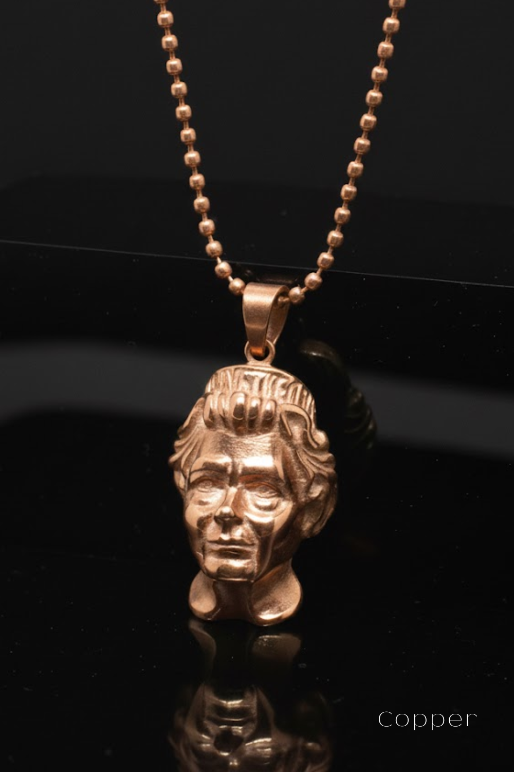A gold-colored pendant in the shape of a human head is displayed against a black background.