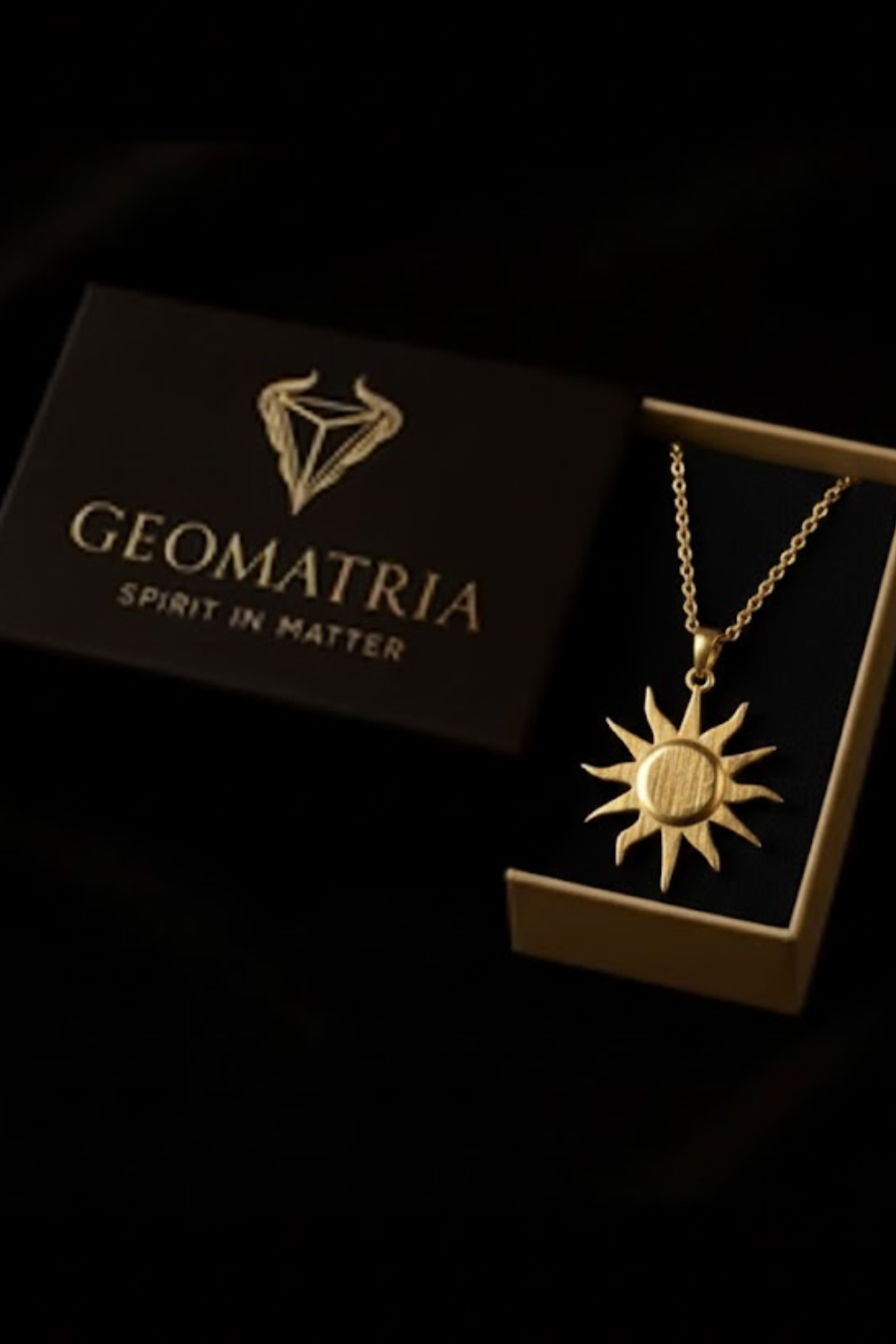 A gold necklace with a sun pendant is displayed in a black box with the text "GEOMATRIA SPIRIT IN MATER" printed on it.