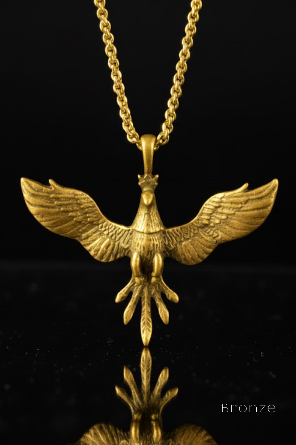 A gold-colored pendant in the shape of a bird, with wings spread wide, is displayed against a black background.