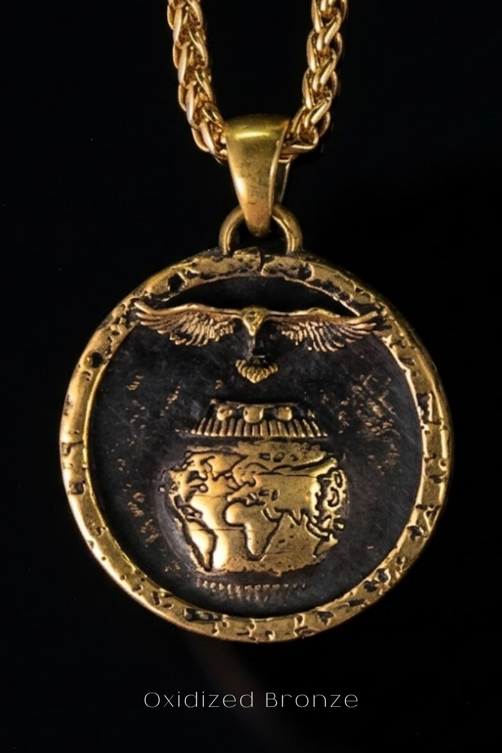 A gold-colored pendant with a detailed design, including a bird, a globe, and a chain, against a black background.