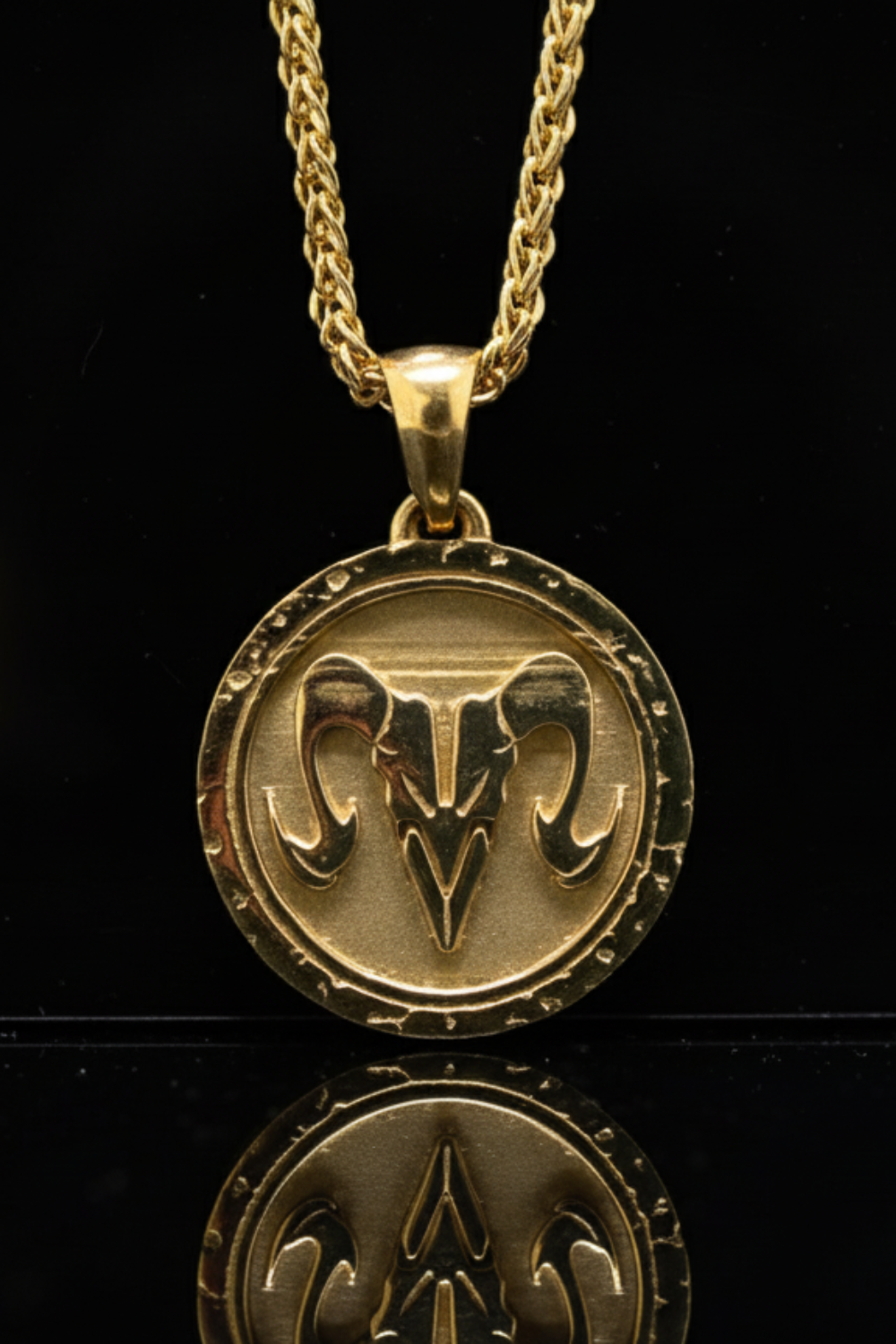 A gold-colored pendant necklace with a circular medallion featuring a ram's head design.