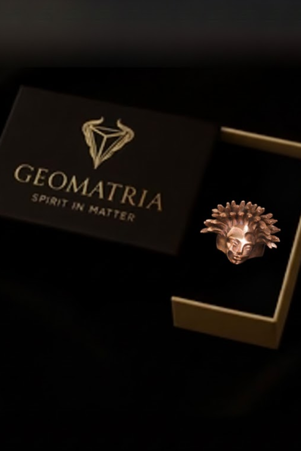 a ring placed inside a box with a gold-colored lid, and the box is labeled "Geomatria Spirit in Matter".