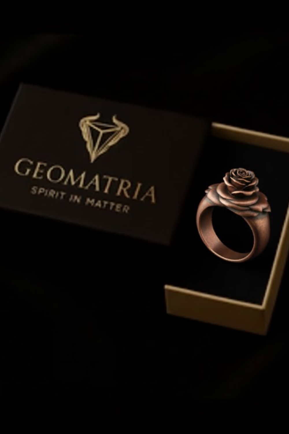 A rose-shaped ring is displayed in a gold box with the text "Geomatria" and "SPIRIT IN MATTERS" printed on it.