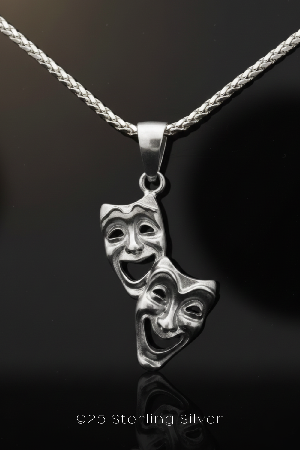 A silver pendant necklace with two silver theatrical masks hanging from a silver chain.