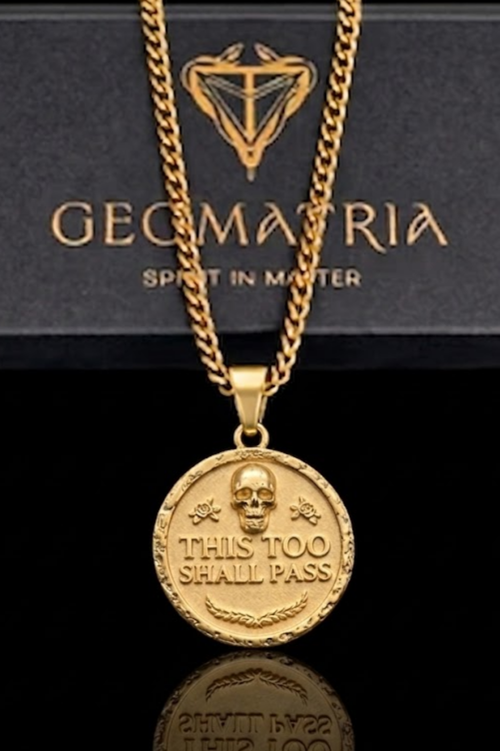 A gold-colored necklace with a pendant featuring a skull and the text "This Too Shall Pass" engraved on it.