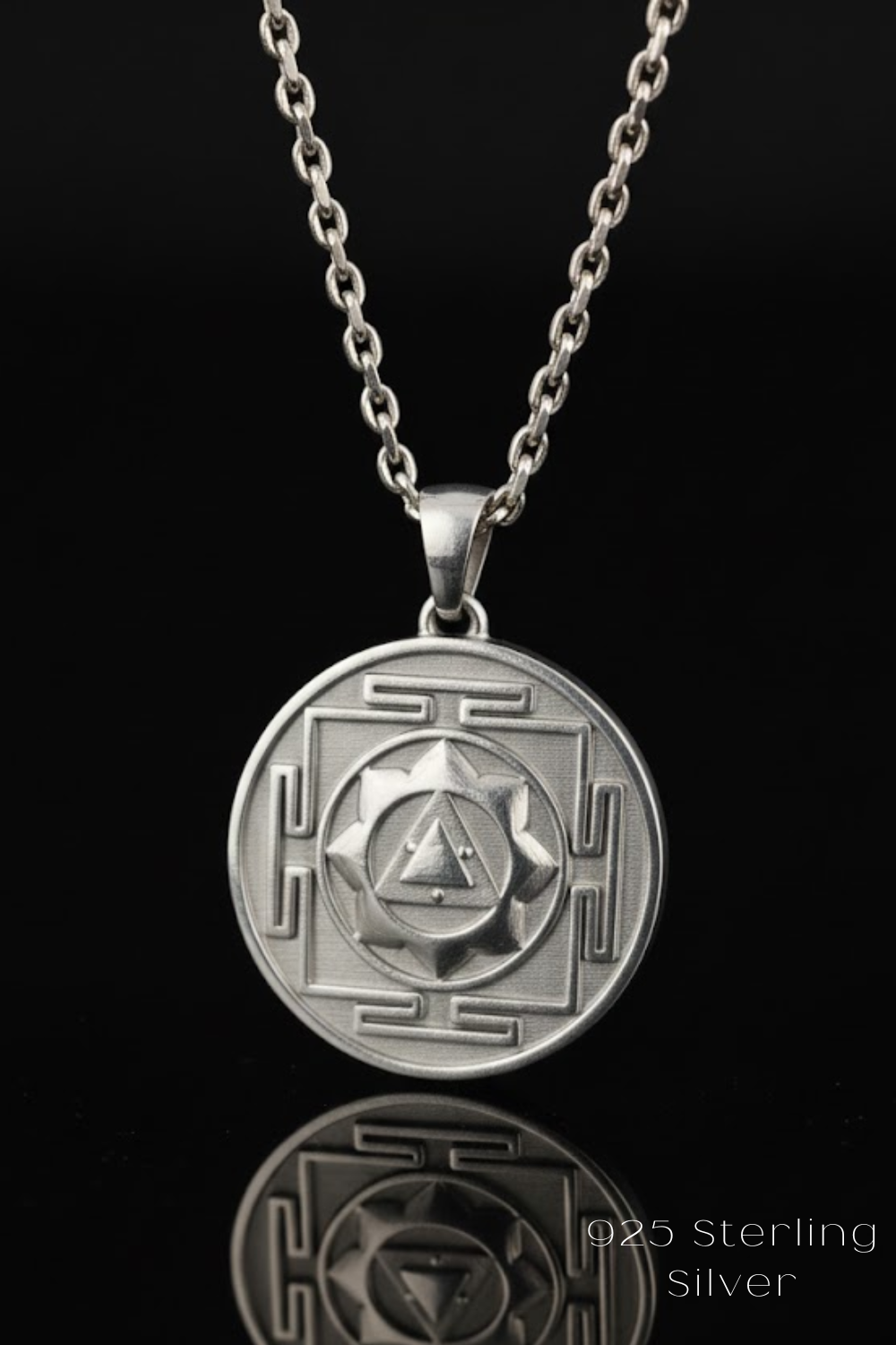 A silver pendant necklace with a circular medallion featuring a geometric design and a triangle symbol.