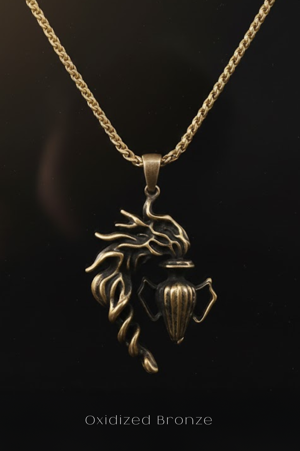 A pendant in the shape of a dragon, made of oxidized bronze, is displayed against a black background.