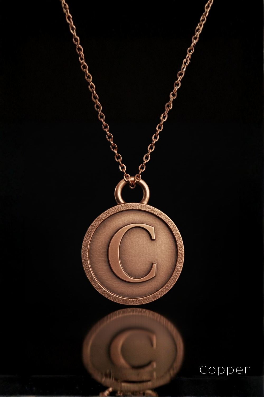 A copper-colored pendant necklace with a large letter 'C' in the center, suspended from a chain against a black background.