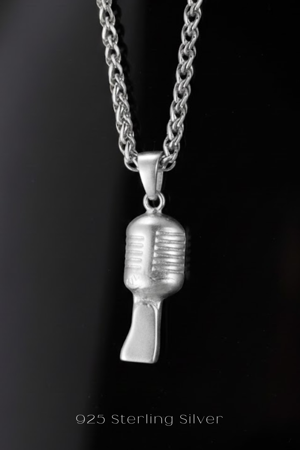 A silver microphone pendant on a necklace against a black background.