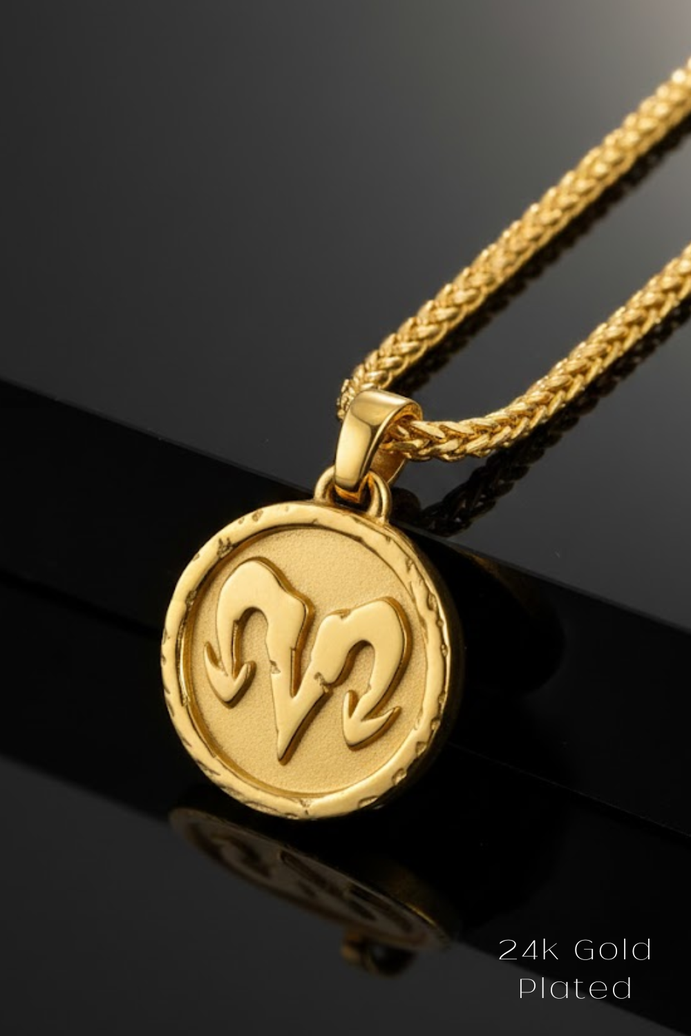 A 24K gold plated pendant featuring a circular medallion with a ram symbol on it, hanging from a gold chain.