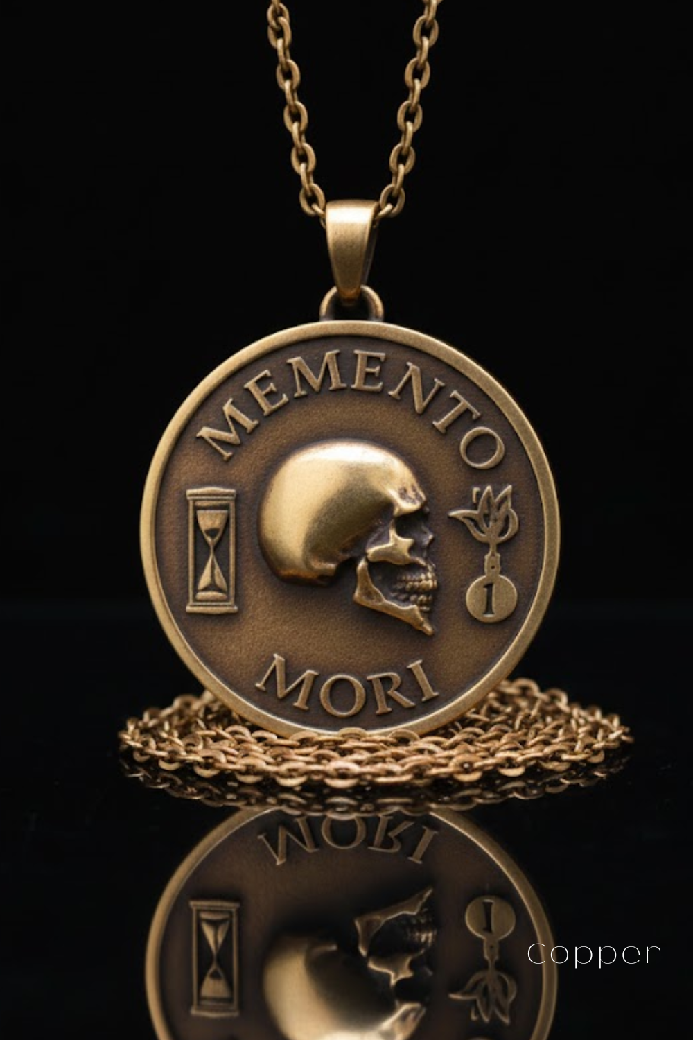 a gold-colored pendant necklace with a circular medallion that has the text "MEMENTO MORI" engraved on it. The pendant is displayed against a black background, and it is reflected in a chain, creating a mirrored effect.