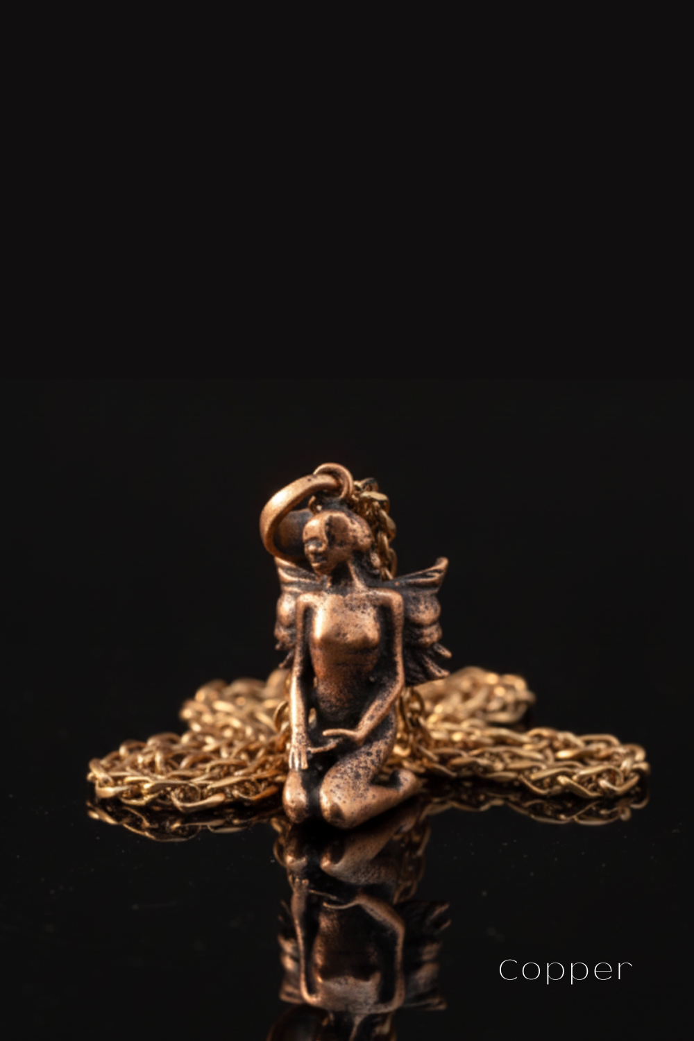 A bronze-colored pendant in the shape of a fairy or mermaid, with wings and a halo, is displayed on a chain against a black background.