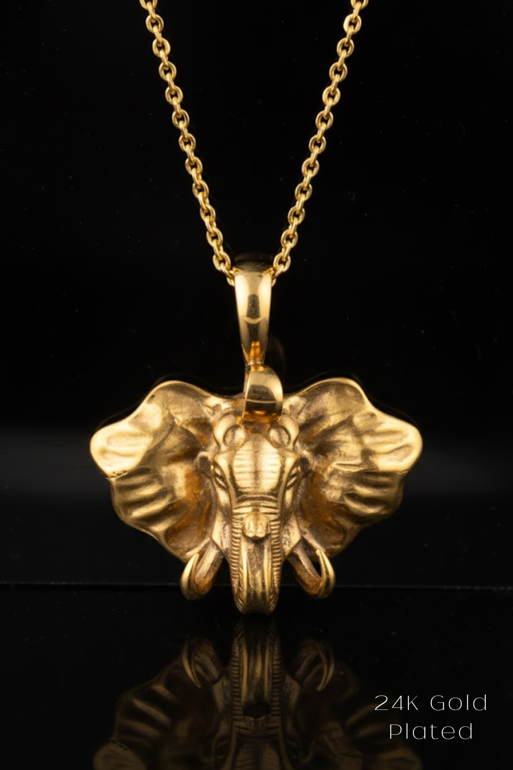 A gold-plated pendant in the shape of an elephant's head is displayed against a black background.