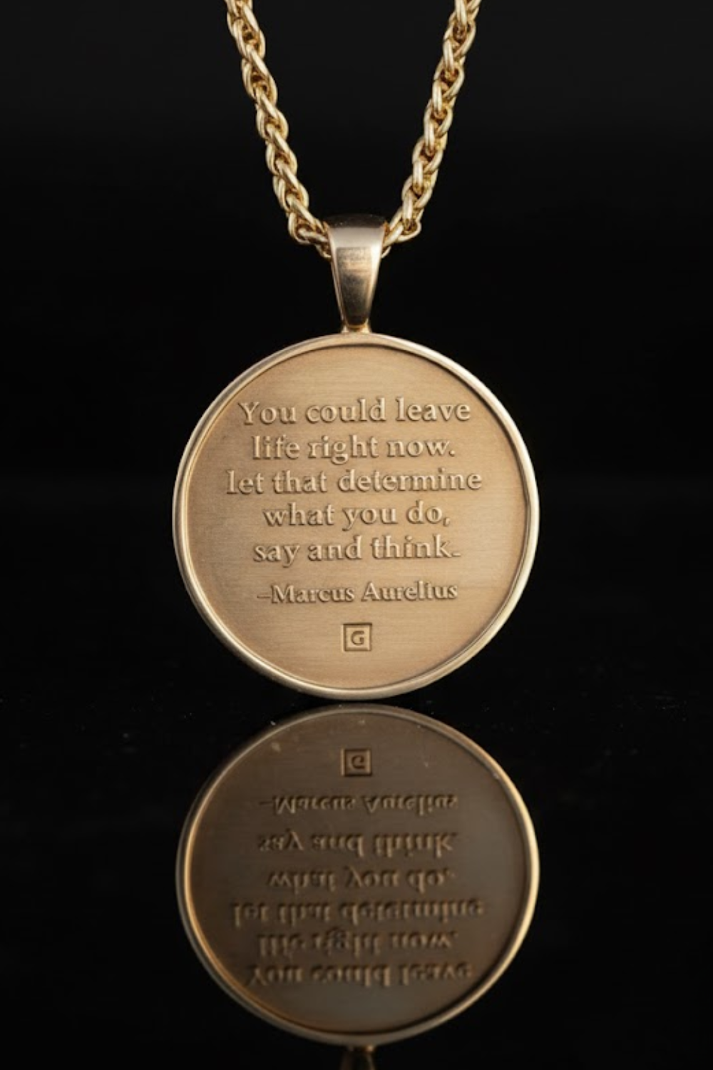A gold-colored pendant necklace with a round medallion-shaped pendant featuring a quote in gold text.