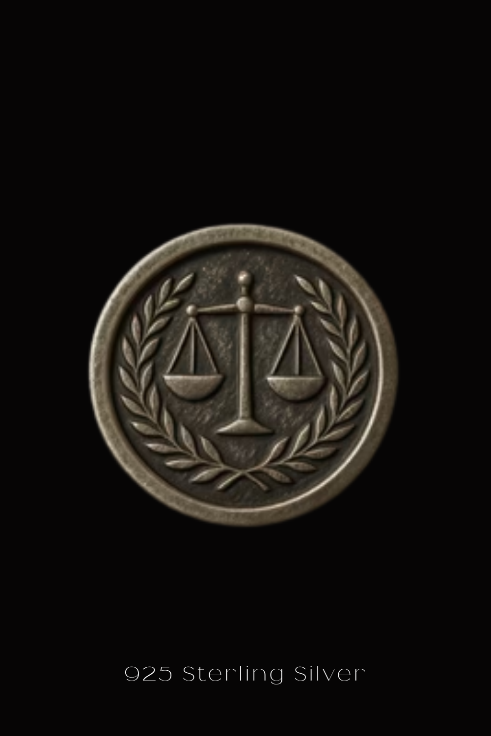 A close-up of a silver-colored metal emblem with a scale and laurel wreath design, against a black background.