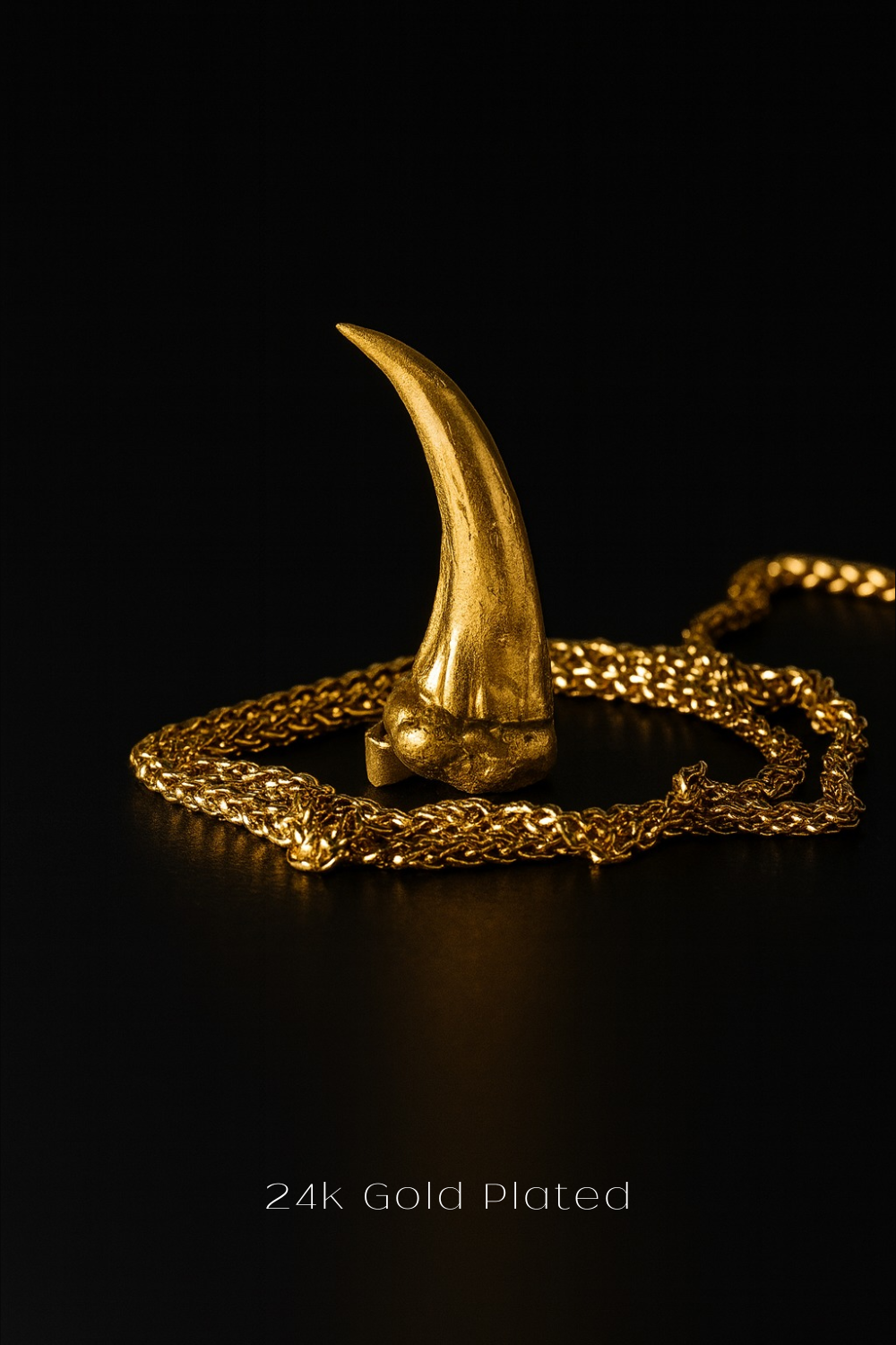 A gold-plated object resembling a claw or talon rests on a gold chain against a black background.