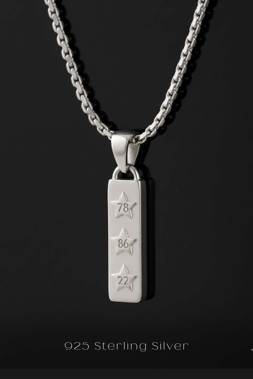 A silver necklace pendant with three stars engraved on it, set against a black background.