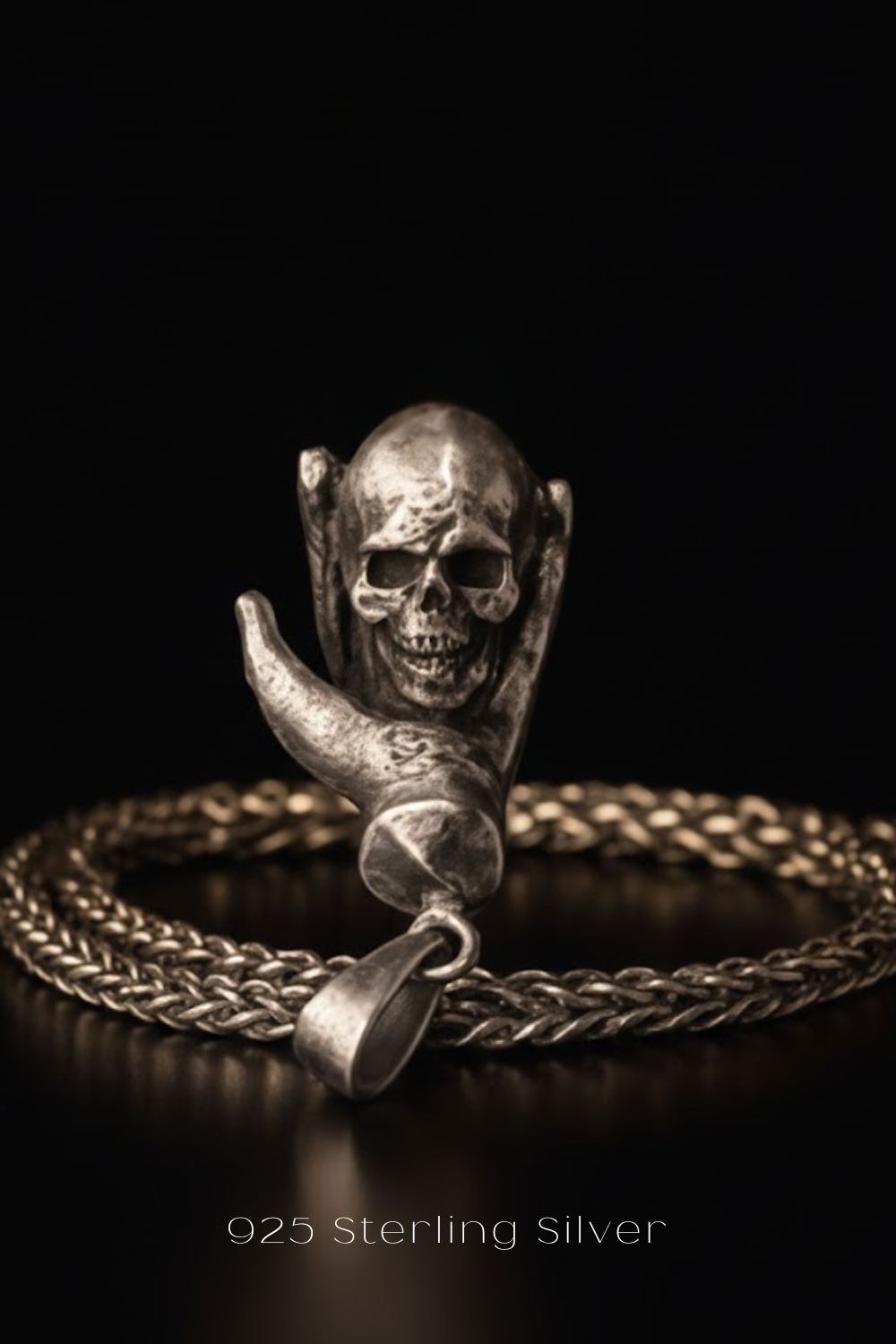 A silver skull pendant with a chain around it, set against a dark background.