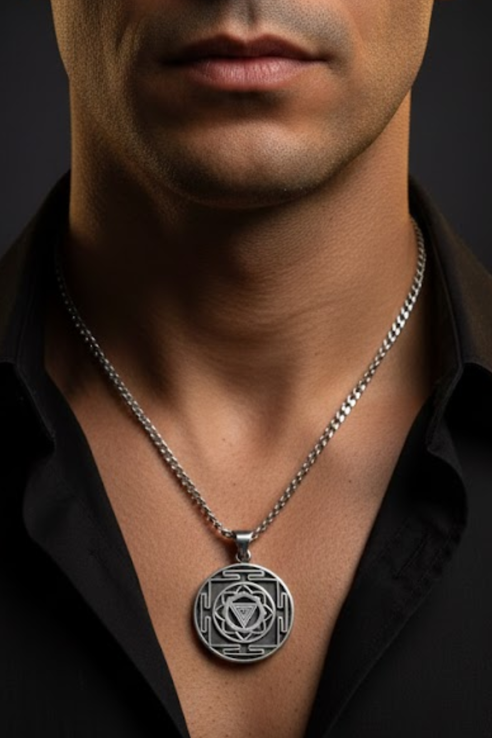 A close-up of a man's neck and chest area, with a silver pendant necklace featuring a circular medallion with a geometric design.