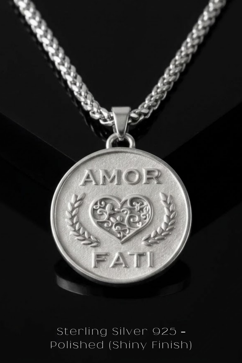 A silver pendant necklace with a heart-shaped medallion featuring the words "Amor Fati" engraved on it.