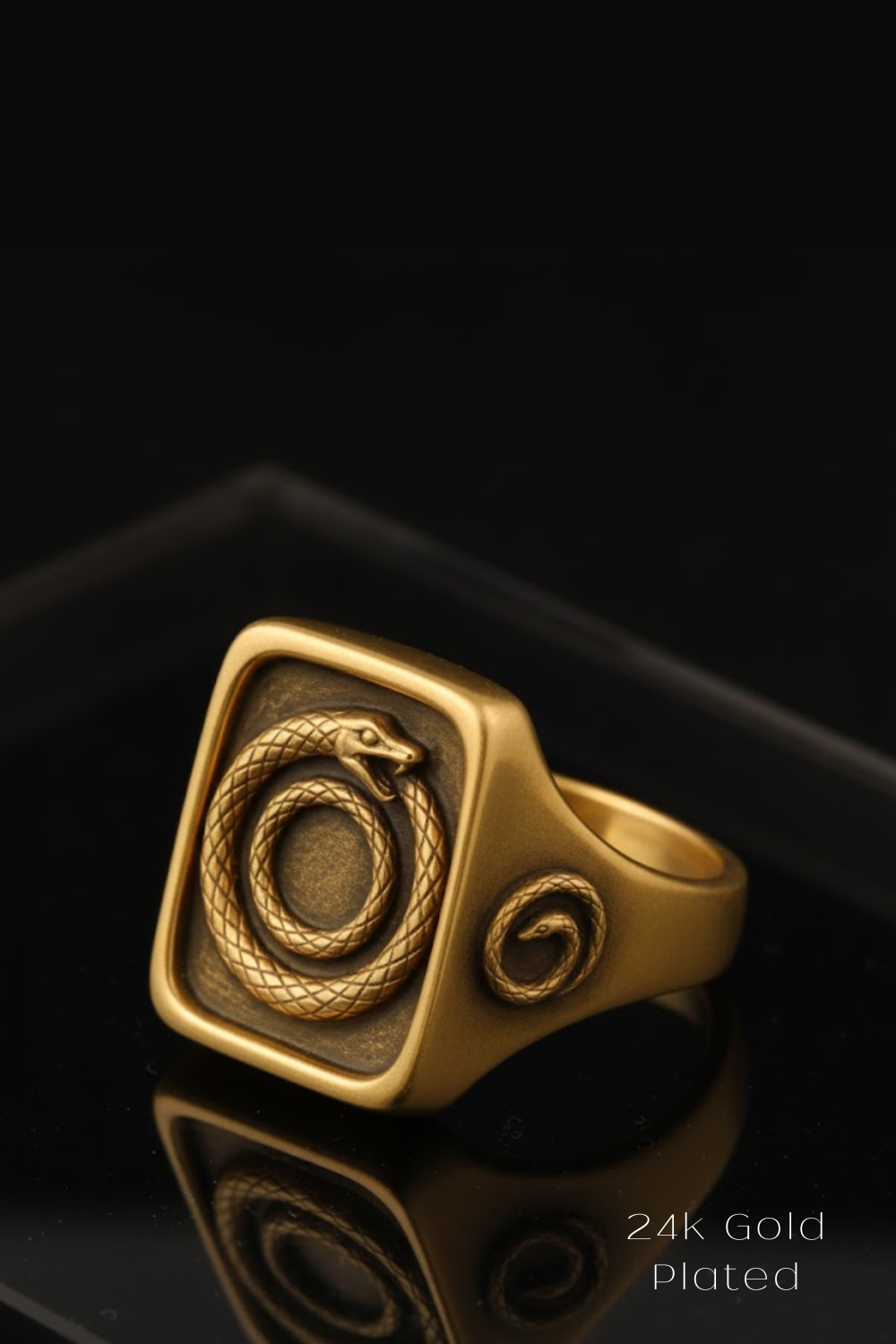 A gold ring with a square-shaped design featuring a snake and a spiral pattern.