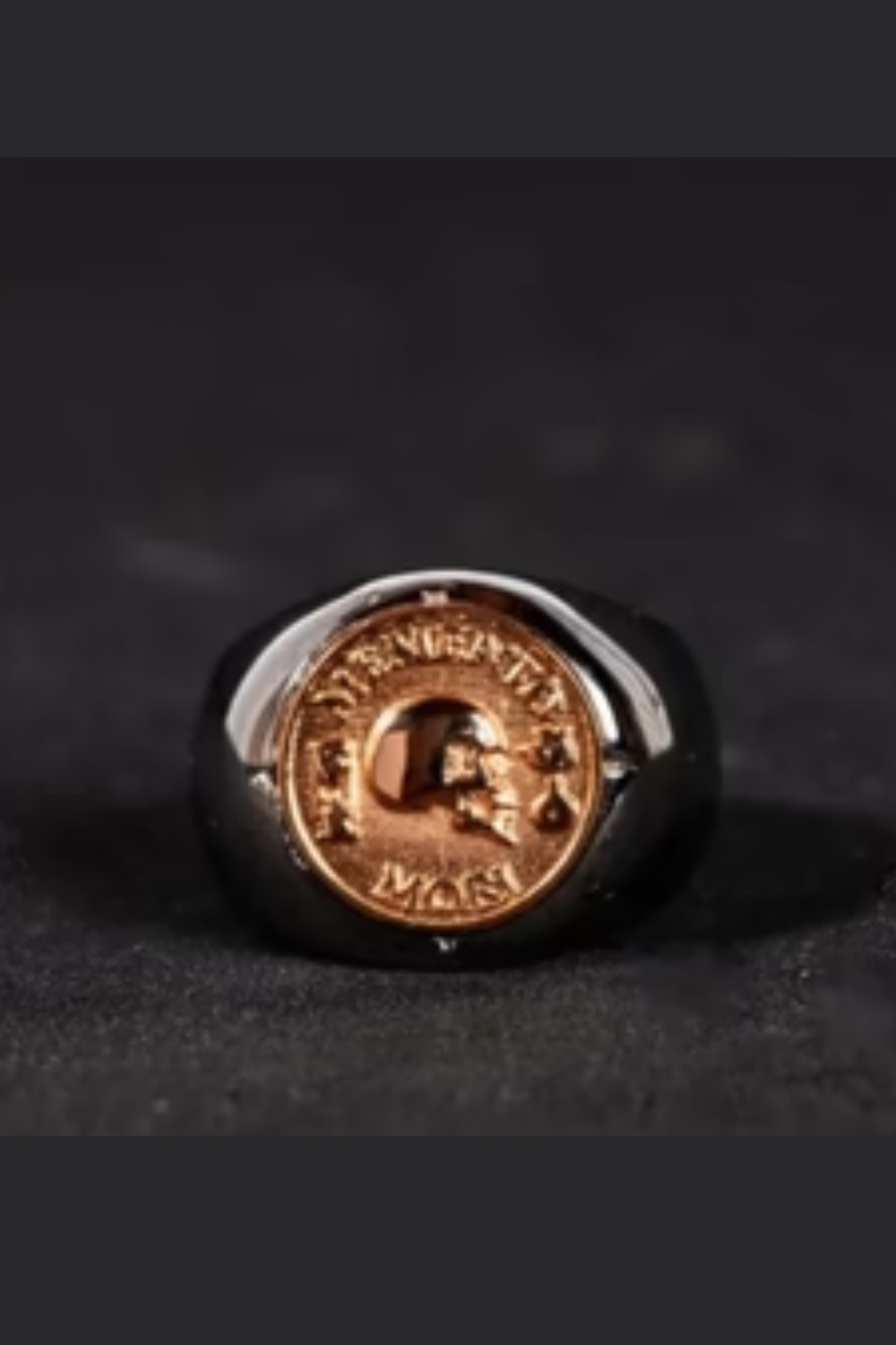 A ring with a gold-colored metal band and a circular design featuring a skull and crossbones symbol.